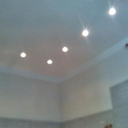 F.U.H Artur LASKOWSKI - Biały sufit z równomiernie rozmieszczonymi, wpuszczanymi lampkami LED, oświetlającymi wnętrze. Widoczny fragment ściany i narożnik pokoju.