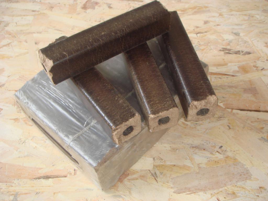 Ułożone brykiety drzewne z otworem w środku, część zafoliowana, na tle płyty OSB. Widoczne detale faktury i struktury brykietów.