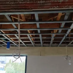 Szkielet sufitu podwieszanego z profili metalowych w trakcie montażu w Lisowicach, widoczne przewody instalacji elektrycznej i fragment okna.