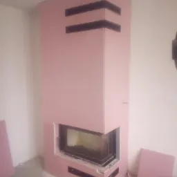 Wnętrze z kominkiem obudowanym płytami kartonowo-gipsowymi w trakcie montażu, widoczne elementy konstrukcyjne i wykończeniowe, surowe ściany i podłoga.