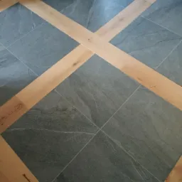 Szara, kwadratowa podłoga z płytek imitujących kamień, przedzielona jasnymi, drewnianymi listwami w kształcie krzyża.