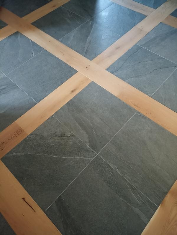 Szara, kwadratowa podłoga z płytek imitujących kamień, przedzielona jasnymi, drewnianymi listwami w kształcie krzyża.