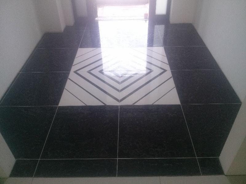 Ułożona podłoga z ciemnych płytek z centralnym wzorem rombu z jasnych płytek. Widok z góry, fuga jasna, błyszcząca powierzchnia.