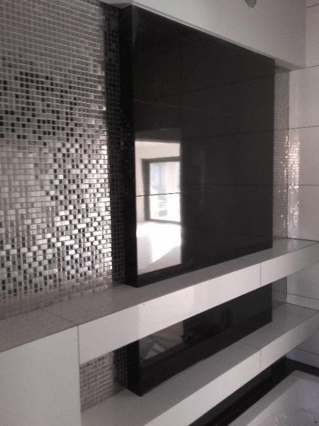 Nowoczesna łazienka w Chojnowie z czarną, szklaną ścianą i mozaiką. Białe półki dodają lekkości wnętrzu. Minimalistyczny design i eleganckie wykończenie.