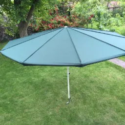 Zielony parasol ogrodowy z metalową konstrukcją na trawniku w Częstochowie. Widok z g&oacute;ry, w tle roślinność i mur.