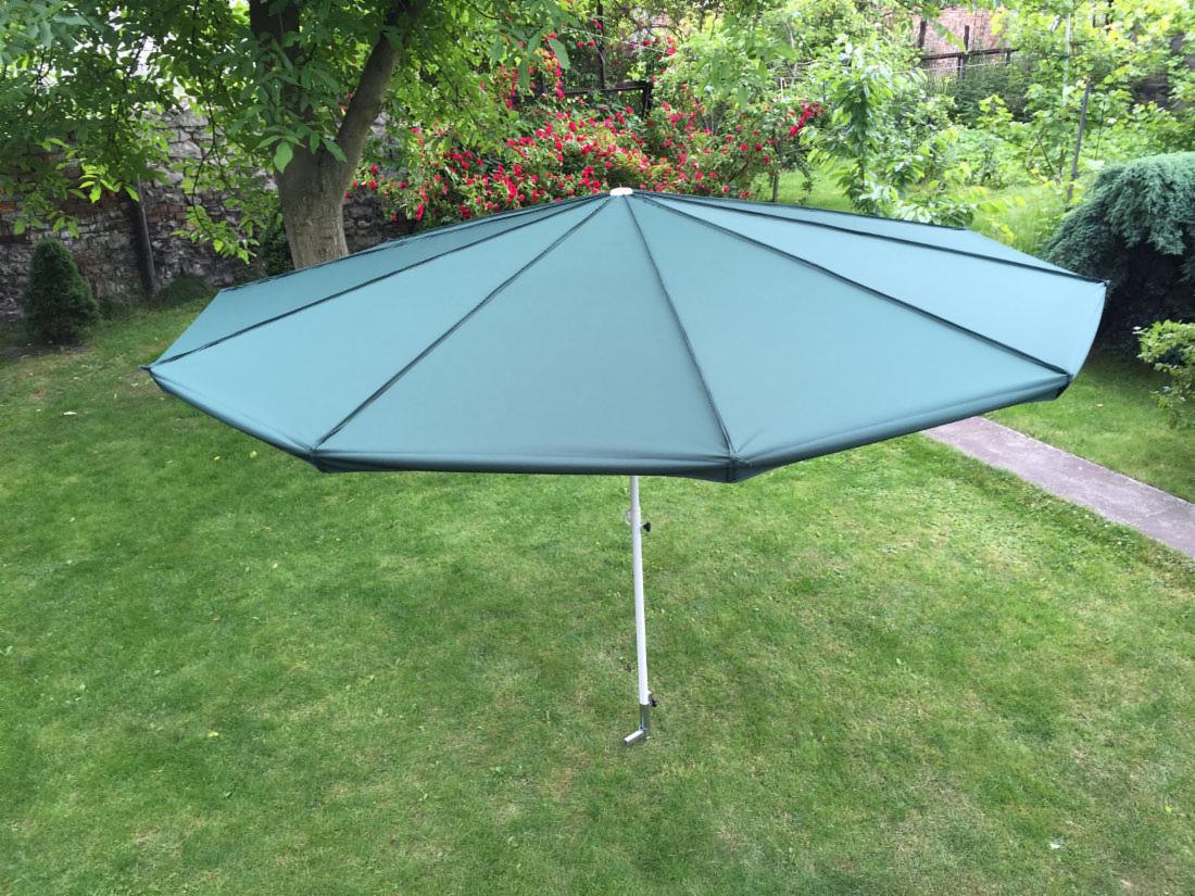 Zielony parasol ogrodowy z metalową konstrukcją na trawniku w Częstochowie. Widok z góry, w tle roślinność i mur.