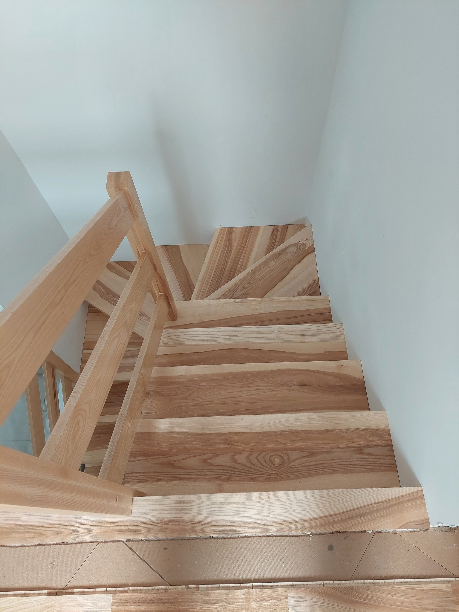 Jasne, drewniane schody z balustradą, widok z góry, ukazujący usłojenie drewna i minimalistyczne wykończenie wnętrza.