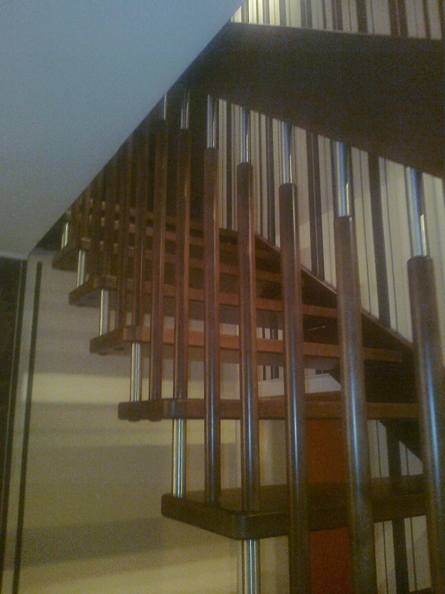 Klatka schodowa z drewnianymi schodami i metalowymi balustradami, widok z dołu, ściana w pionowe pasy w tle.