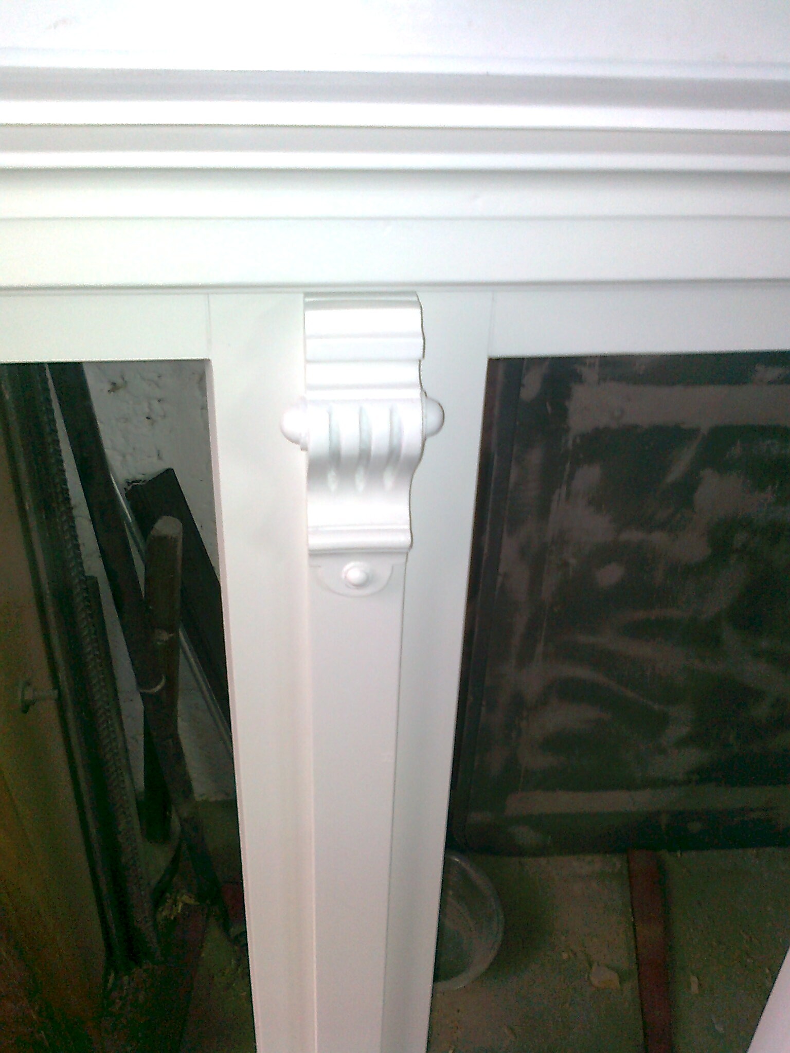 Fragment białej, zdobionej ramy okiennej lub drzwiowej w Rydzynie, widoczne narzędzia i ślady prac remontowych w tle.