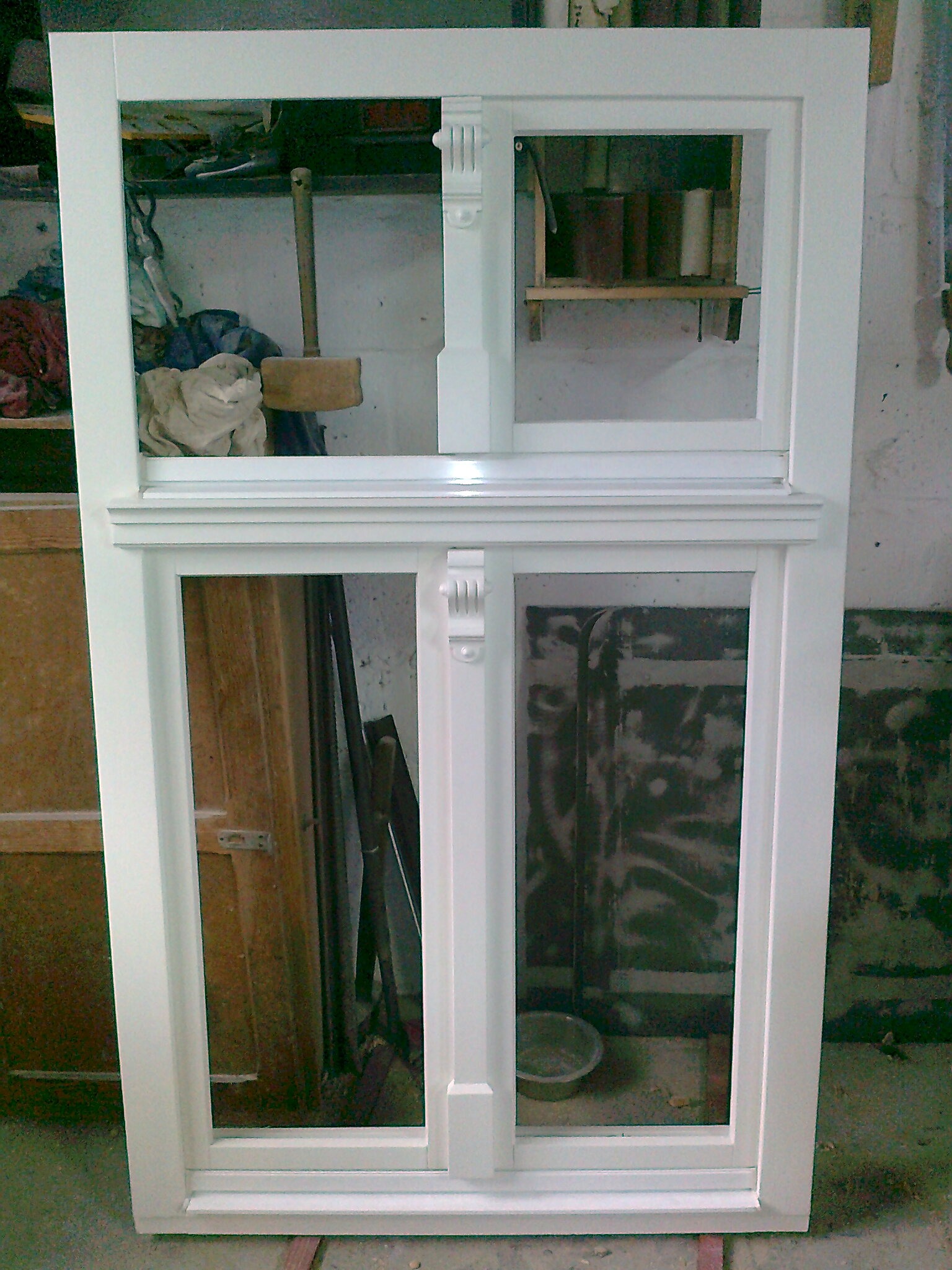 Biała, drewniana rama okienna z dekoracyjnymi elementami, widoczna w warsztacie z narzędziami i materiałami w tle.