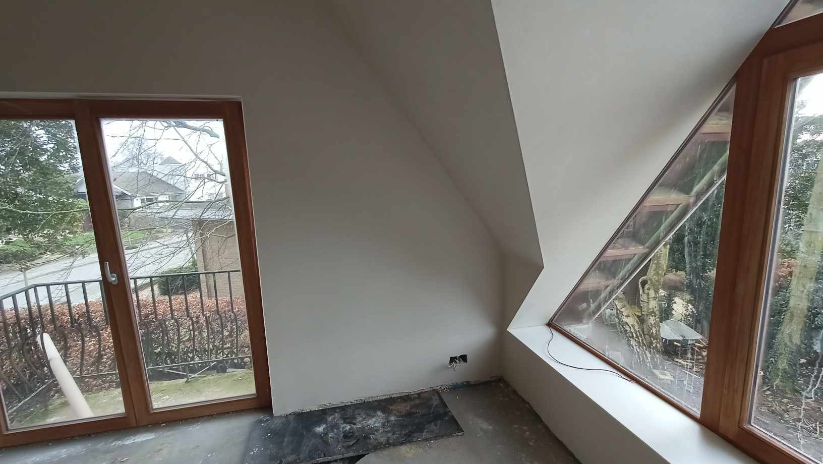 Gładkie, jasne ściany poddasza po nałożeniu gładzi w Jazowsku, widoczne okna drewniane o nietypowym kształcie i zabezpieczona podłoga.