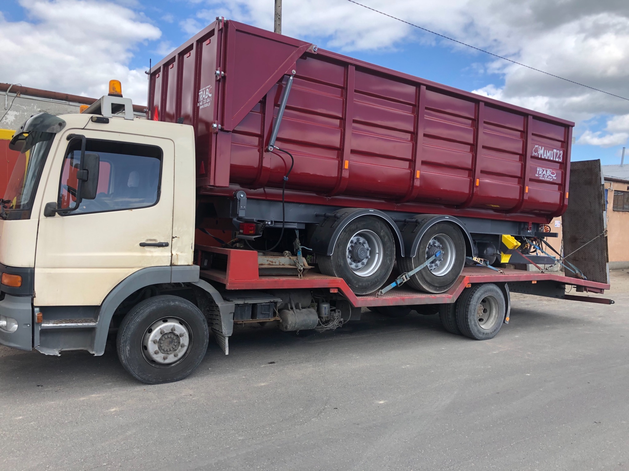 Ciężarówka z nową, bordową zabudową skrzyniową typu wywrotka, z widocznym logo 'MAMUT23' i 'TRABO', zaparkowana na asfaltowej drodze.