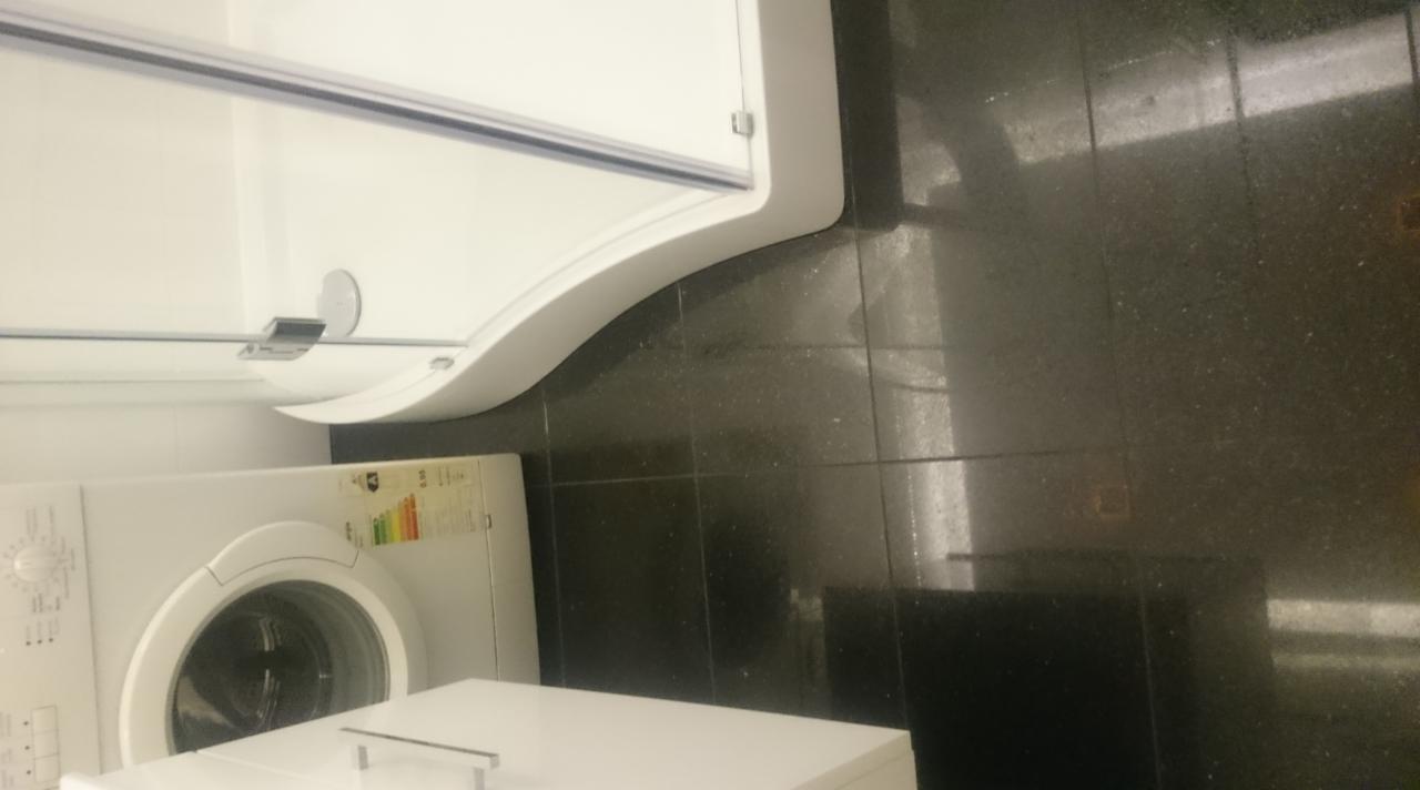 Nowoczesna łazienka z czarnymi płytkami, białą kabiną prysznicową z zaokrąglonym profilem i pralką. Widok na fragment wykończonego wnętrza.