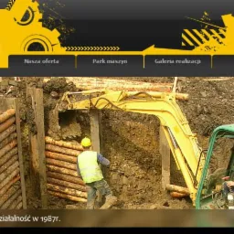 Żółta koparka w trakcie prac ziemnych przy zabezpieczonym wykopie. Widoczny pracownik w kamizelce odblaskowej i operator w kabinie koparki.