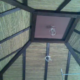 Wnętrze dachu z trzciny i ciemnego drewna, widok z dołu, z wiszącymi kablami oświetleniowymi i fragmentem rusztowania.