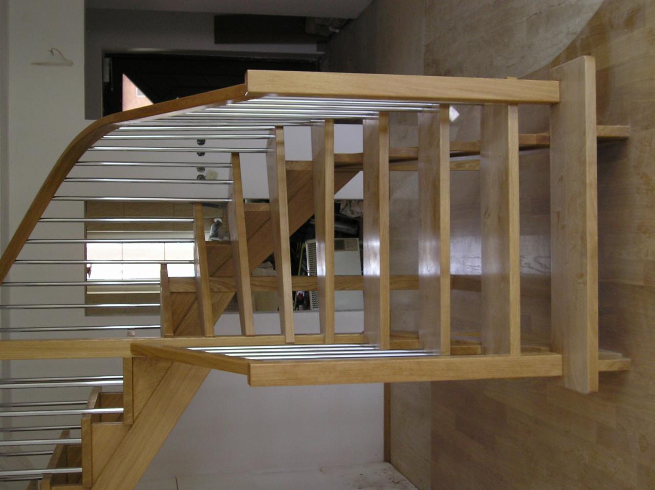 Nowoczesne schody z jasnego drewna z metalowymi prętami, widok z dołu, ukazujący konstrukcję i detale wykończenia.