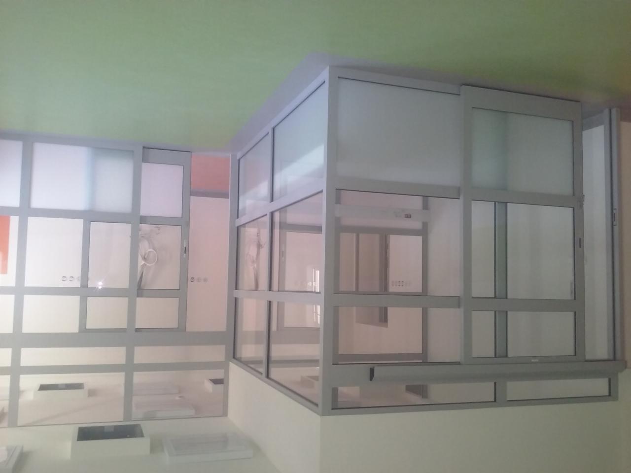 Nowoczesna zabudowa szklana z aluminiowymi ramami, tworząca ściankę działową w biurze. Widoczne przesuwne drzwi i matowe szkło zapewniające prywatność.