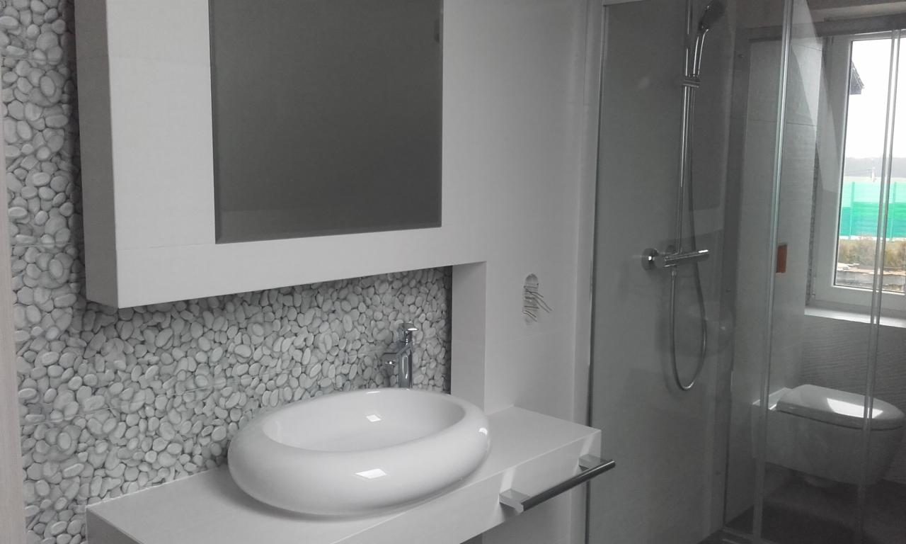 Nowoczesna łazienka z umywalką nablatową o owalnym kształcie, bateria chromowana, ściana wyłożona mozaiką z białych otoczaków, kabina prysznicowa ze szklanymi drzwiami i widocznym fragmentem...