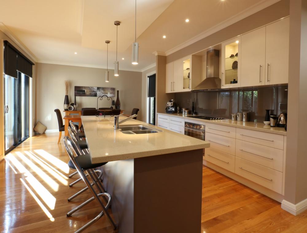 Jasna kuchnia z wyspą i drewnianą podłogą; światło słoneczne wpada przez przesuwne drzwi balkonowe, oświetlając parkiet.