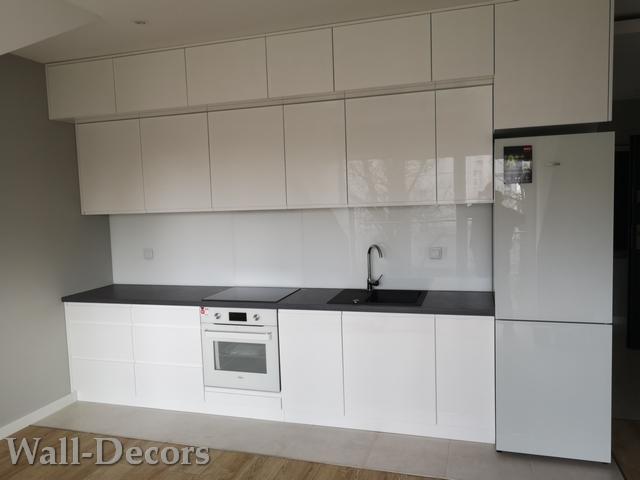 Nowoczesna, biała kuchnia z górnymi szafkami pod sufit, czarnym blatem, płytą indukcyjną i piekarnikiem w zabudowie oraz lodówką po prawej stronie.