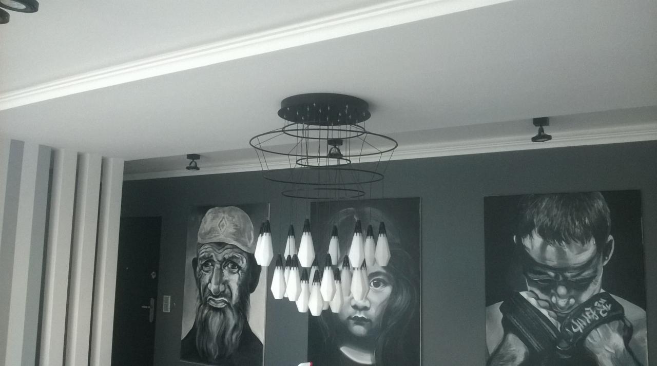 Nowoczesny żyrandol z geometrycznymi kloszami w salonie z szarymi ścianami i trzema czarno-białymi portretami.