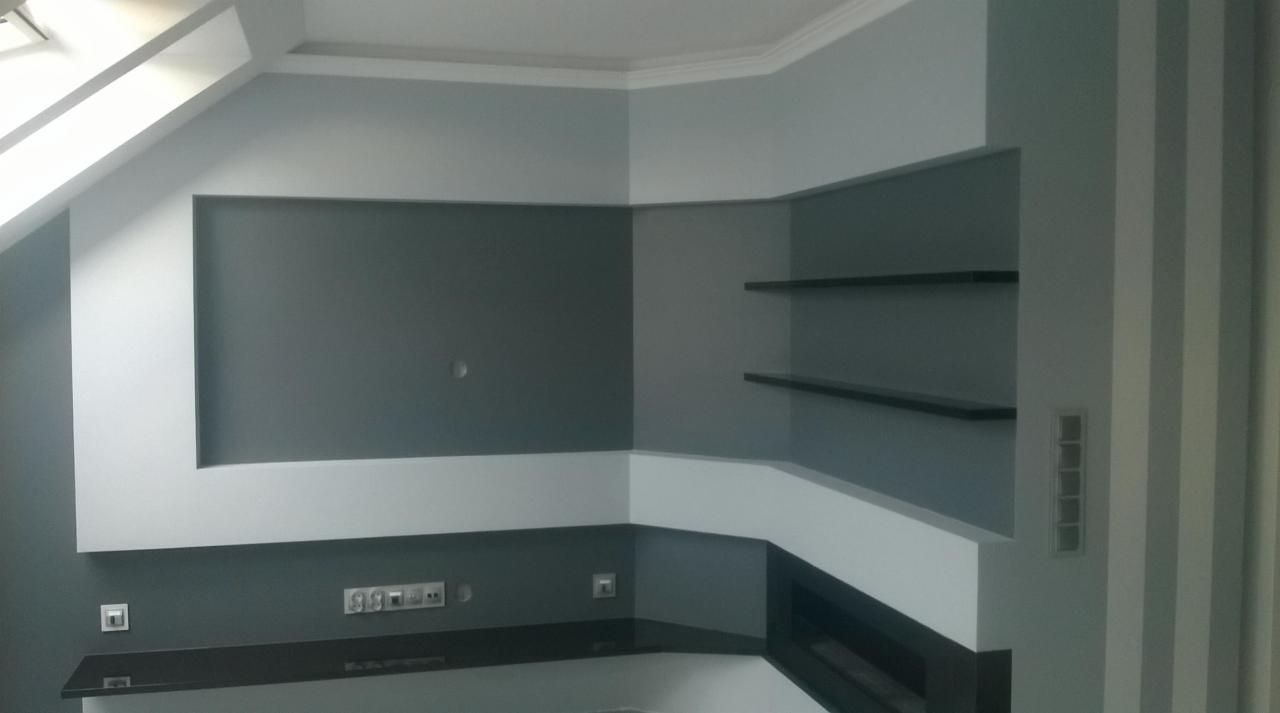 Nowoczesne wnętrze w Nowej Jastrząbce z szaro-białymi ścianami, półkami i wnęką na ścianie pod skosem, widoczne gniazdka elektryczne.