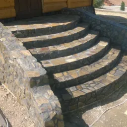 Wykończone kamienne schody wejściowe do drewnianego domu z widoczną instalacją elektryczną na słupie