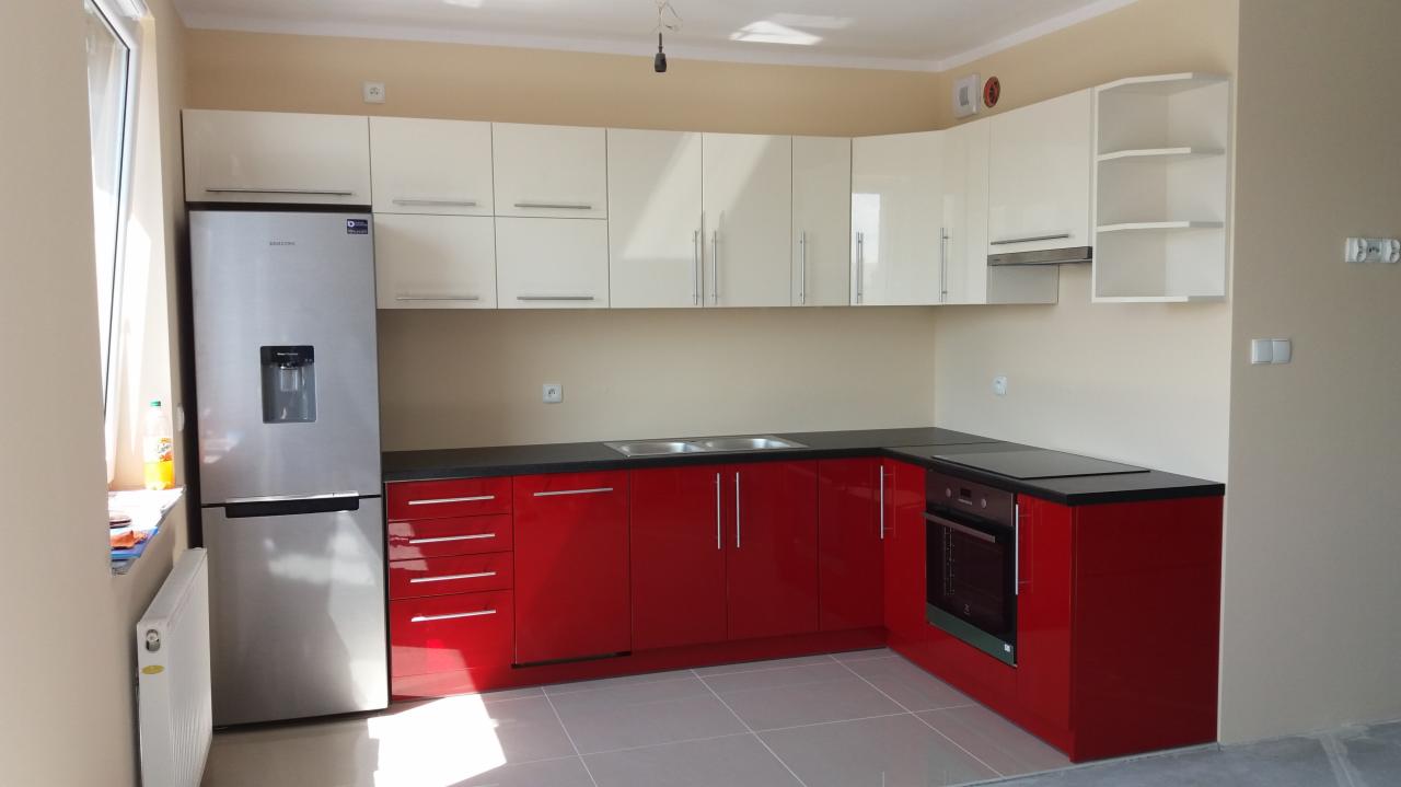 Nowoczesna kuchnia z białymi górnymi szafkami i czerwonymi dolnymi, czarnym blatem i srebrną lodówką.