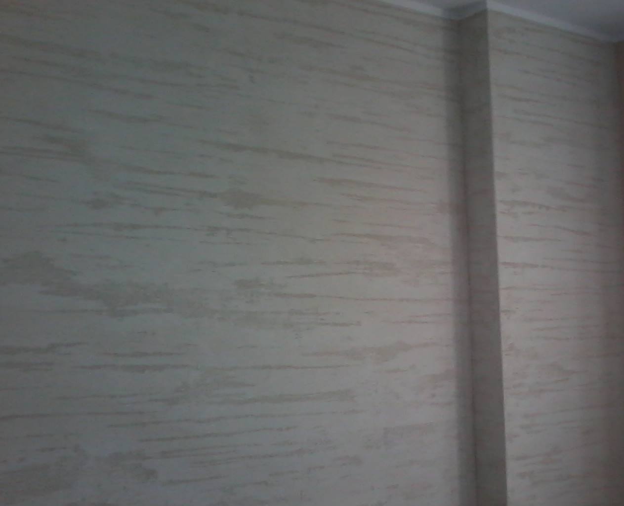 Ściana wewnętrzna z dekoracyjnym tynkiem w odcieniach beżu, z widoczną pionową krawędzią ściany po prawej stronie.