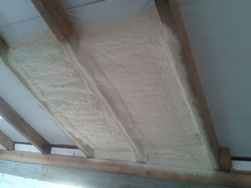 Szczelnie wypełniona przestrzeń poddasza jasną pianą izolacyjną, widoczne drewniane elementy konstrukcyjne dachu.