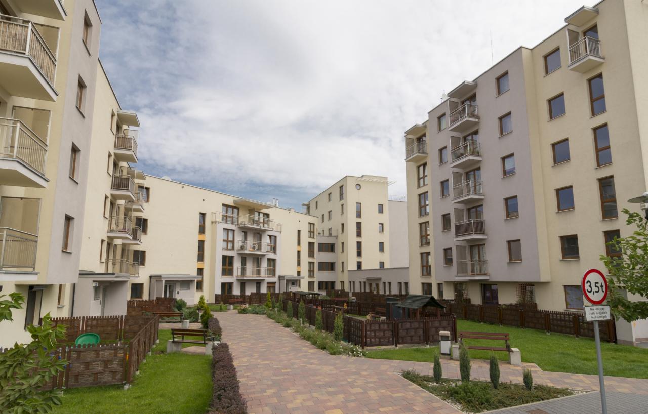 Kompleks nowoczesnych budynków mieszkalnych z balkonami, placem zabaw i zielonymi przestrzeniami, widok z poziomu chodnika.
