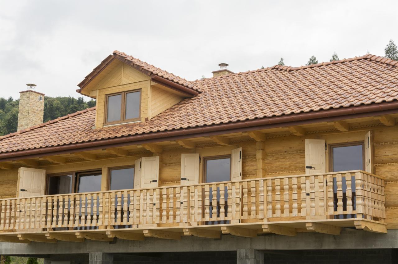 Drewniany dom z balkonem w Krakowie, widok z dołu. Czerwona dachówka i jasne drewno tworzą spójną całość. Otwarte okiennice dodają uroku.