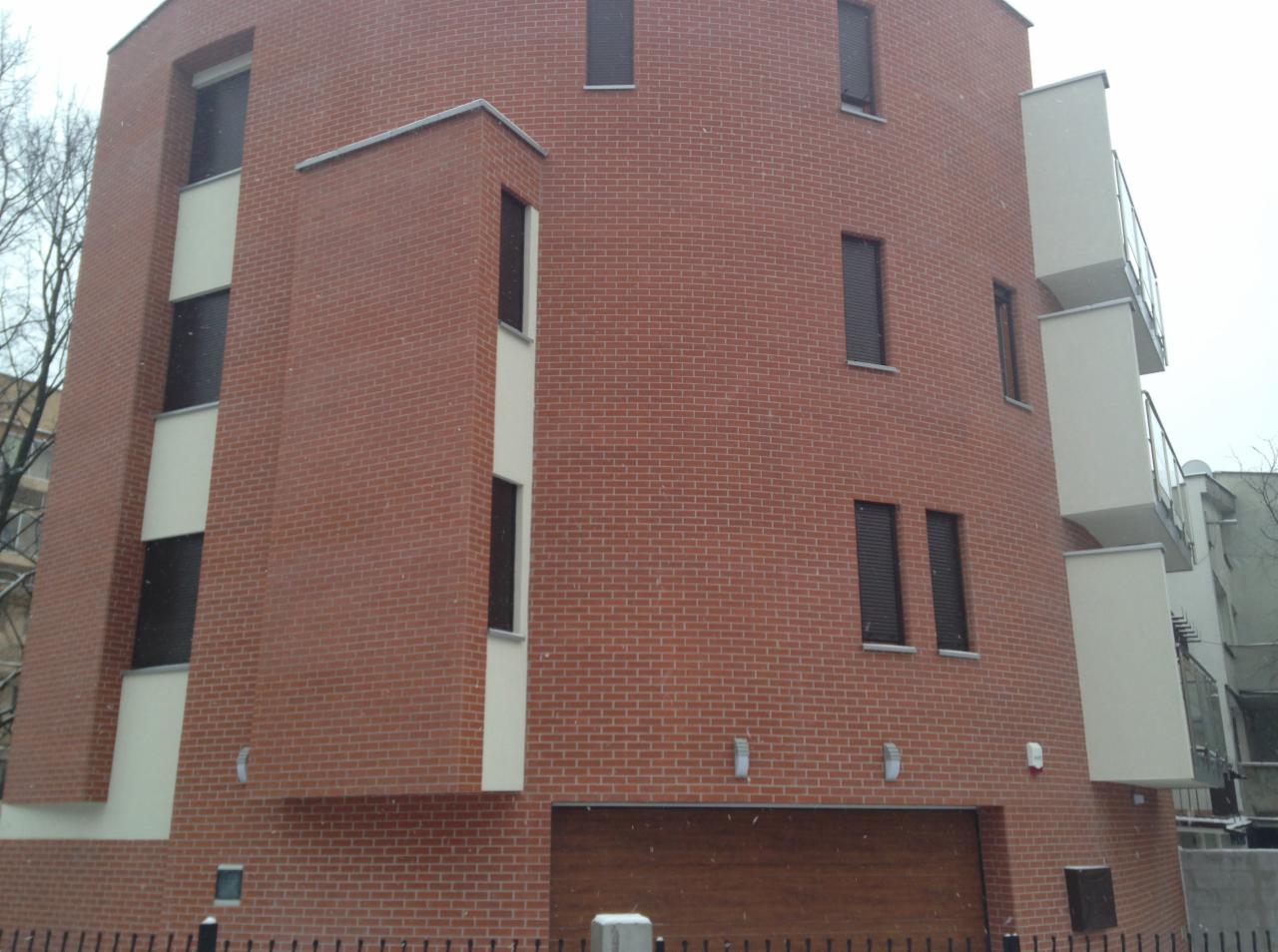 Nowoczesny budynek z czerwonej cegły z drewnianą bramą garażową i balkonami, widziany z niskiego kąta w pochmurny dzień.