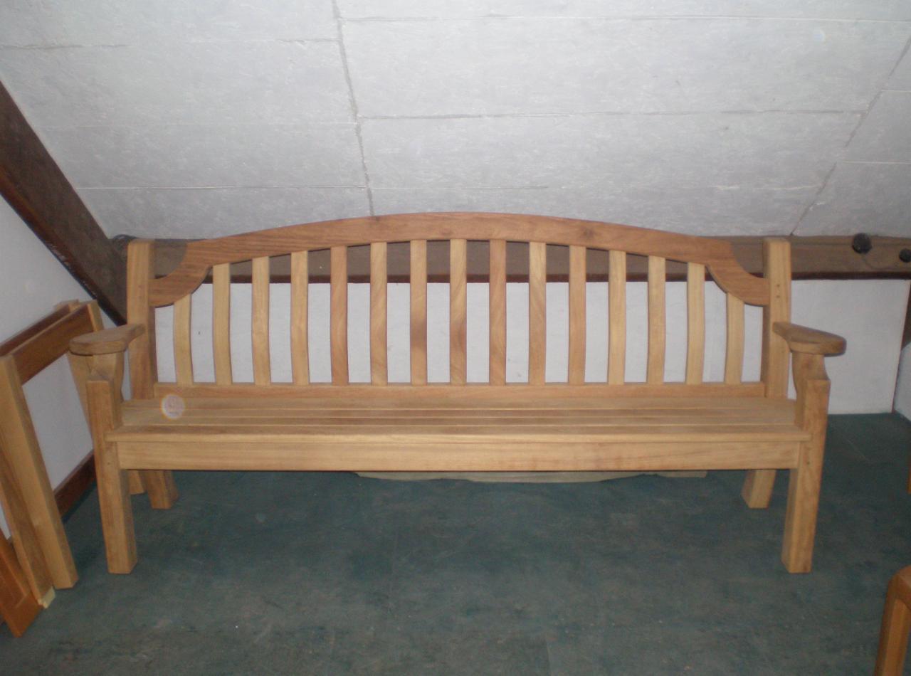 Drewniana ławka ogrodowa z oparciem szczebelkowym, wykonana z jasnego drewna, sfotografowana w pomieszczeniu z niskim sufitem i widoczną konstrukcją więźby dachowej.