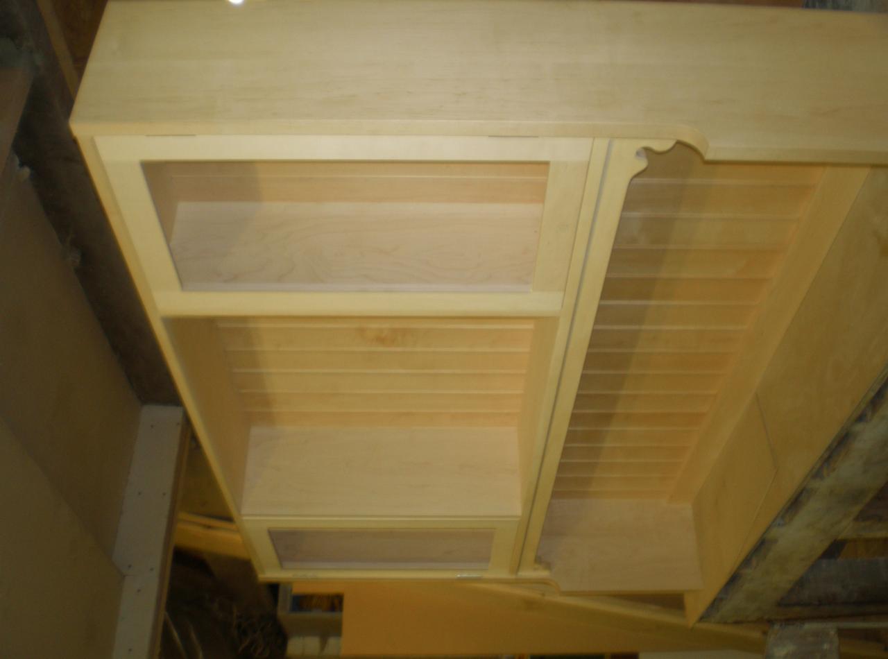 Jasna, drewniana zabudowa z półkami, widoczna od dołu, z dekoracyjnym wykończeniem krawędzi. Element konstrukcyjny w trakcie montażu.