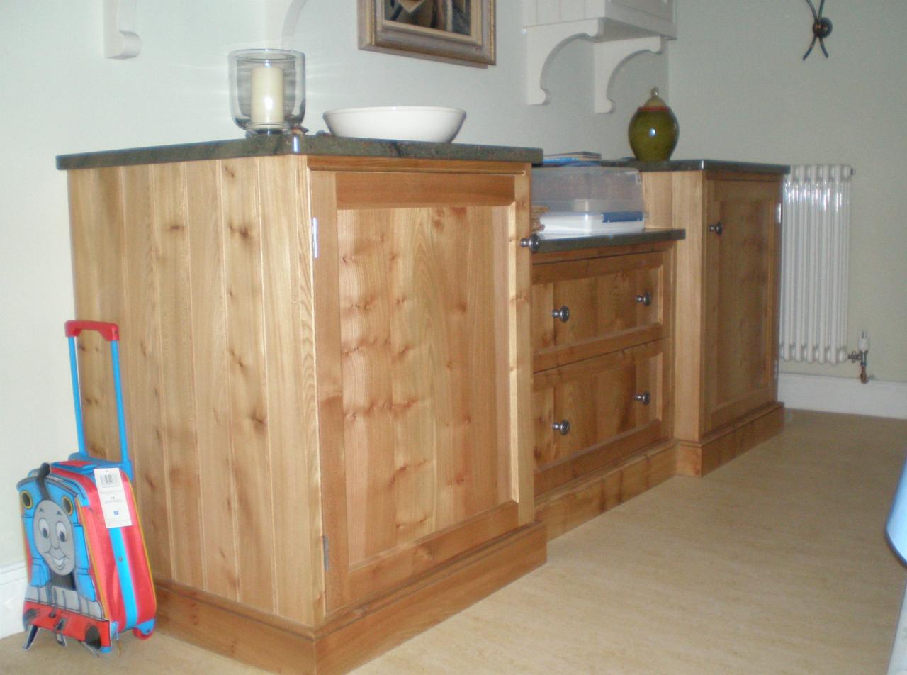 Drewniana komoda z szufladami i szafką w jasnym odcieniu drewna, z ciemnym blatem, uzupełniona o dekoracje i walizkę dla dziecka.