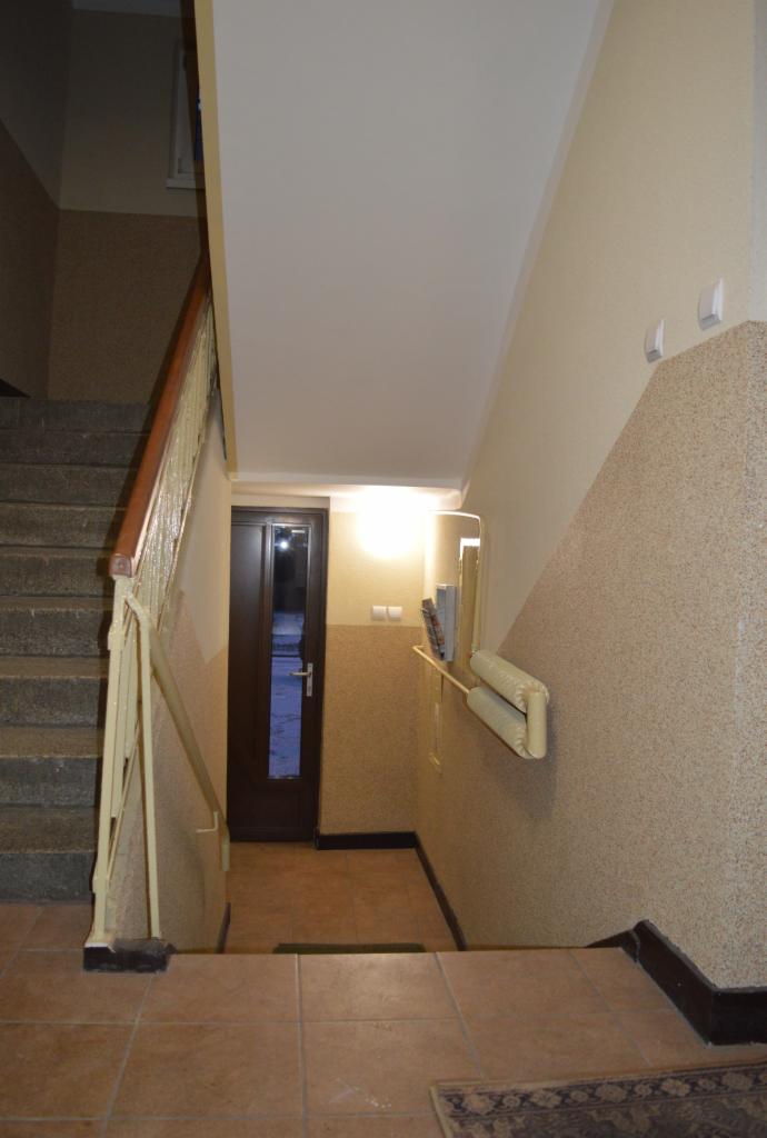 Klatka schodowa w budynku wielorodzinnym po remoncie: odnowione ściany z fakturą, nowe płytki na podłodze i schodach, lampy na ścianie. Widok z góry na dół.