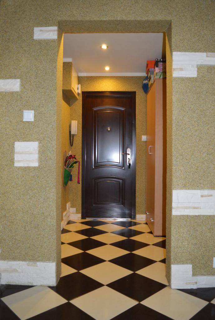 Korytarz po remoncie: wzorzysta podłoga, dekoracyjne ściany z elementami imitującymi kamień, ciemne drzwi wejściowe, szafa na buty.