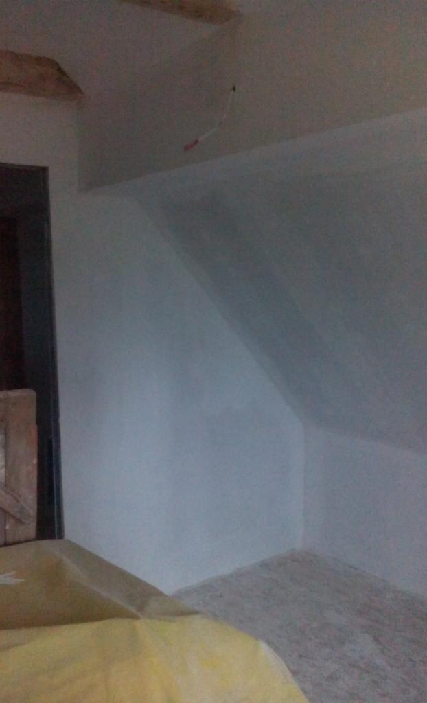 Poddasze po remoncie: świeżo pomalowane ściany w odcieniach szarości, widoczne drewniane belki stropowe i wystający przewód elektryczny. Ukończone gładzie.