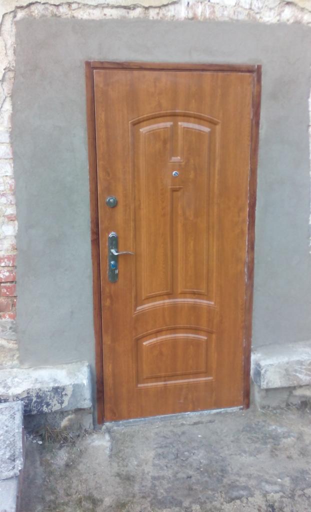Brązowe, zewnętrzne drzwi wejściowe po montażu, osadzone w świeżo otynkowanym murze. Widoczna klamka i wizjer.