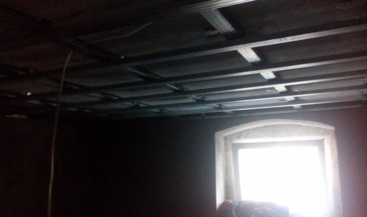 Szkielet sufitu podwieszanego z metalowych profili w trakcie montażu, widok z wnętrza, Mirsk. Okno w tle.