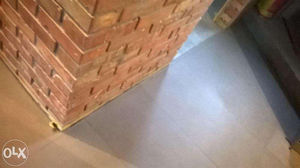 Wykończenie ściany cegłą klinkierową i szara, gładka podłoga. Fragment pomieszczenia z dekoracyjnym wykończeniem. Widok z góry, oświetlenie dzienne.