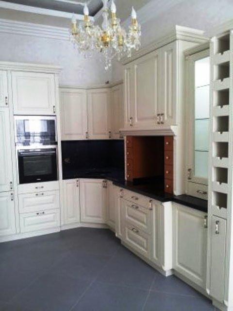 Elegancka kuchnia w stylu klasycznym: kremowe szafki z frezowanymi frontami, czarny blat, zabudowana piekarnik i kryształowy żyrandol.