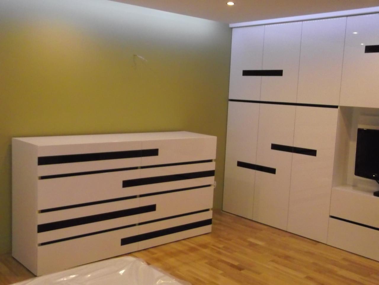 Biała komoda i szafa wnękowa z czarnymi, poziomymi paskami w nowoczesnym salonie z parkietem. Minimalistyczny design, oświetlenie punktowe.