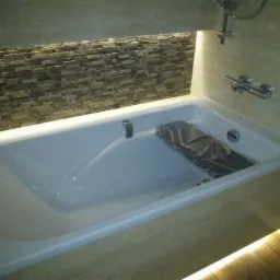 Nowoczesna łazienka z wanną obudowaną płytkami imitującymi drewno, mozaika na ścianie i podświetlenie LED. Bateria wannowa chromowana.