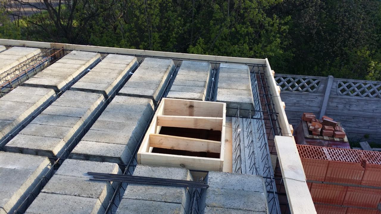 Konstrukcja stropu Teriva z betonowymi pustakami i zbrojeniem stalowym, widoczny drewniany szalunek otworu w stropie, w tle zielone drzewa i szary płot.