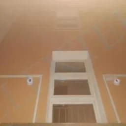 Dwa białe, okrągłe czujniki monitoringu CCTV zamontowane symetrycznie po bokach okna na elewacji budynku. Ujęcie z dołu, lekko zniekształcające perspektywę.