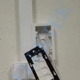 Biała puszka natynkowa z zamontowanym gniazdem sieciowym LAN w czarnej ramce, widoczne okablowanie, montaż na ścianie.