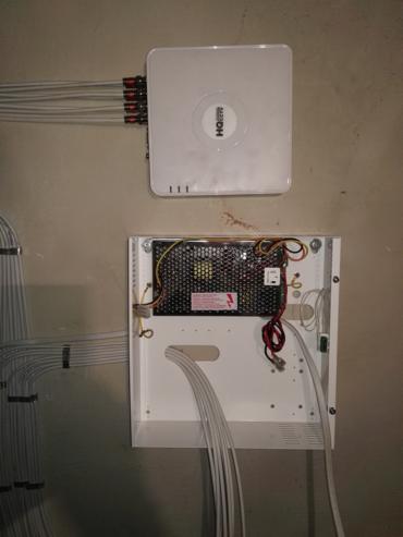 Centrala monitoringu CCTV z podłączonymi kablami, zamontowana na ścianie, widoczny zasilacz w obudowie.