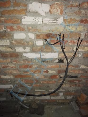 Kable elektryczne wystające ze ściany z cegły, widoczne ślady po kuciu, przygotowanie do montażu rozdzielni.